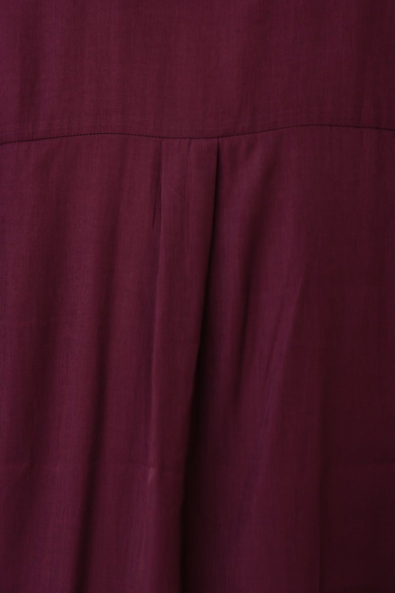 Close-up of a burgundy fabric with subtle pleats, showcasing its rich texture and elegant design.
