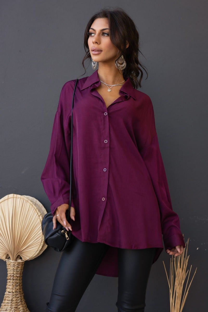 Model wearing a deep plum satin button-up shirt with a relaxed fit, styled with black pants and accessories.
