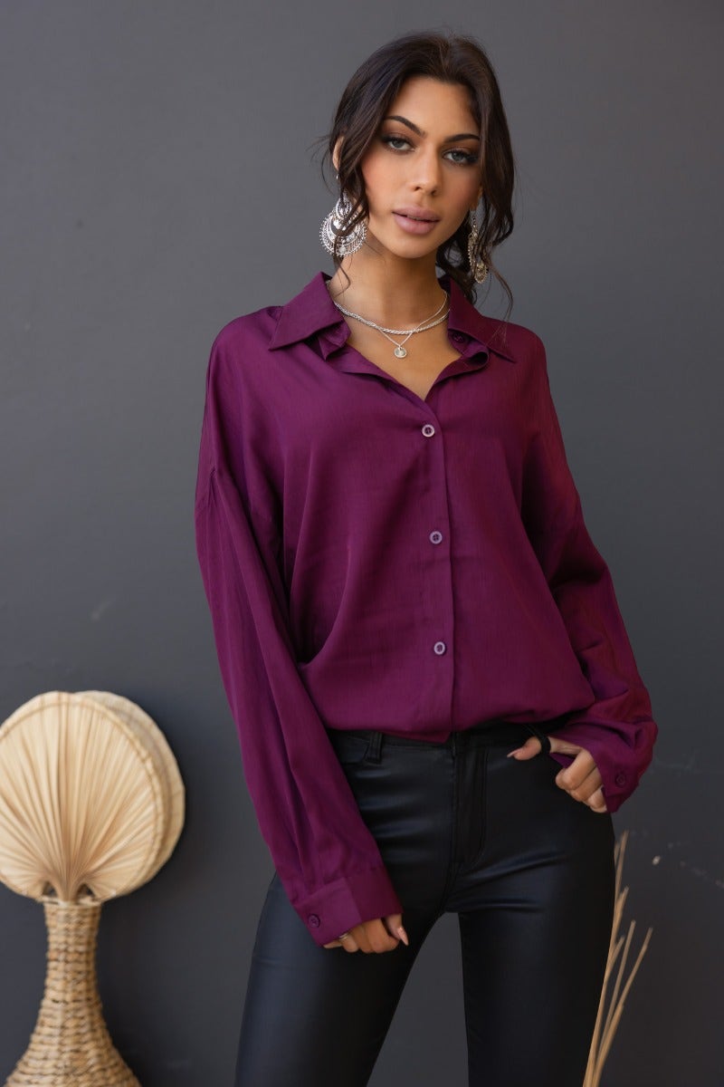 Model wearing a relaxed fit burgundy Nori Top, a satin button-up shirt with a collar, styled with black pants.
