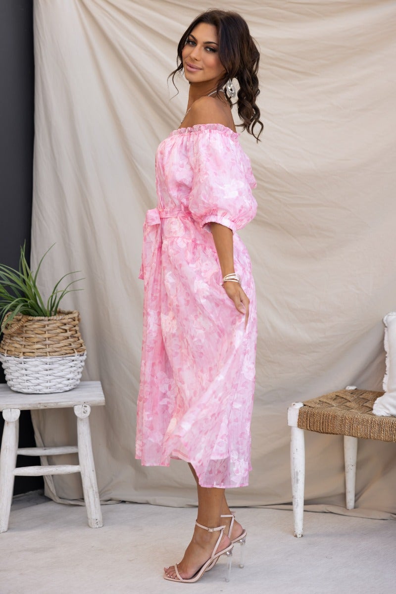 Model wearing a pink embossed print midi dress with off-the-shoulder neckline and removable fabric belt.