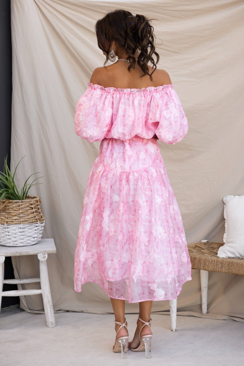 Back view of a pink embossed print midi dress with off-the-shoulder neckline and puff sleeves.
