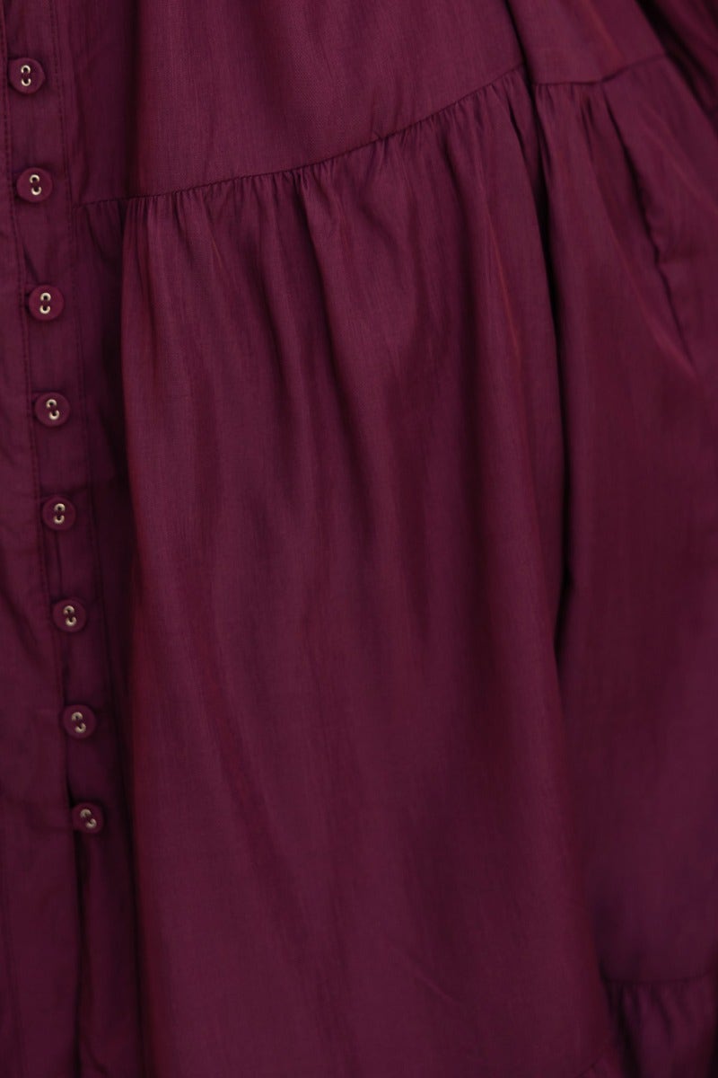 Close-up of the button-up front of an exquisite midi dress in deep burgundy fabric, featuring gathered detailing.