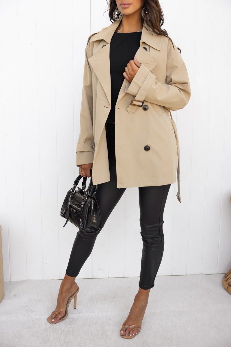 Model wearing the Andie Jacket in beige with a button-up front, styled with black pants and a mini bag.