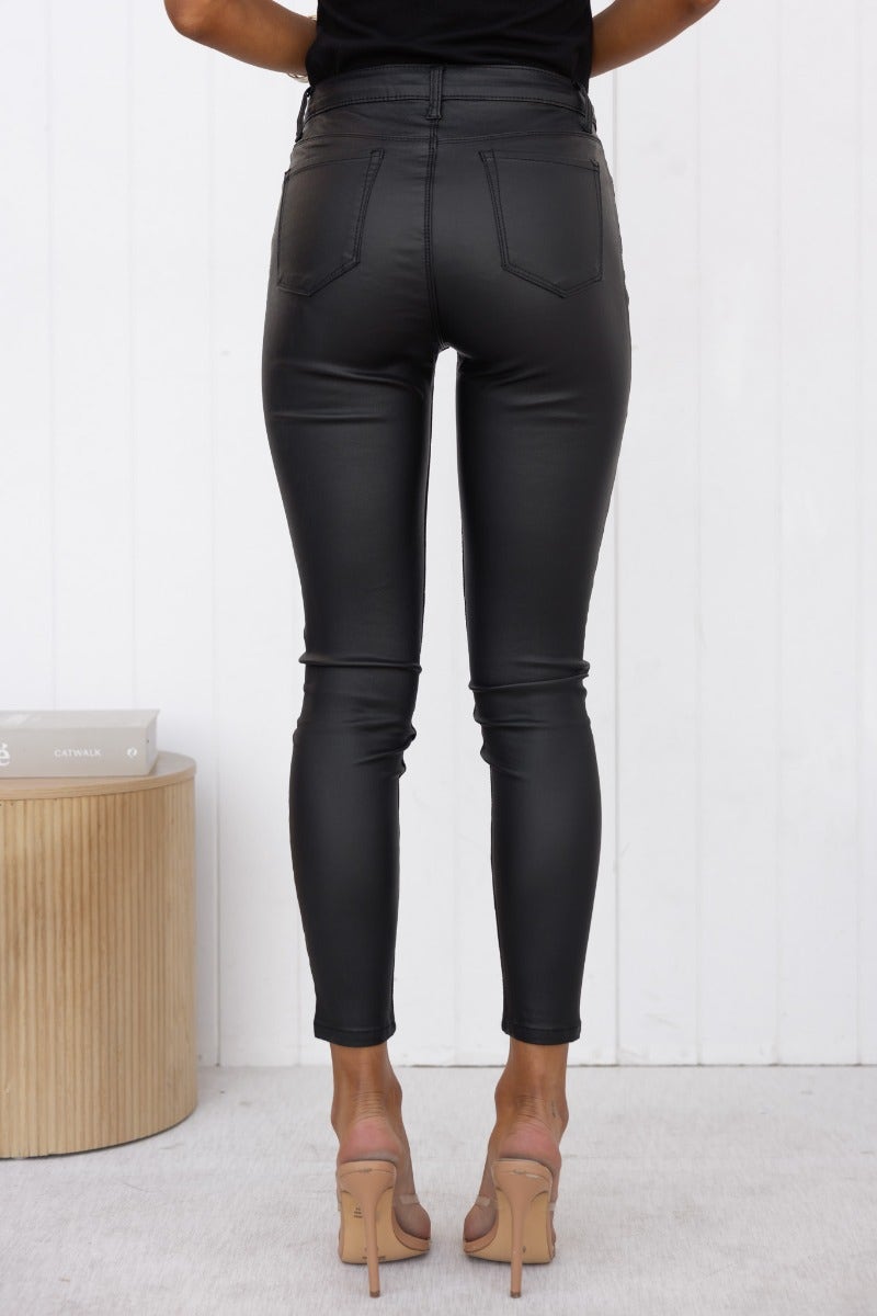 Back view of Harston pants in wet look black with mid-high waist fit and pockets, styled with heels.