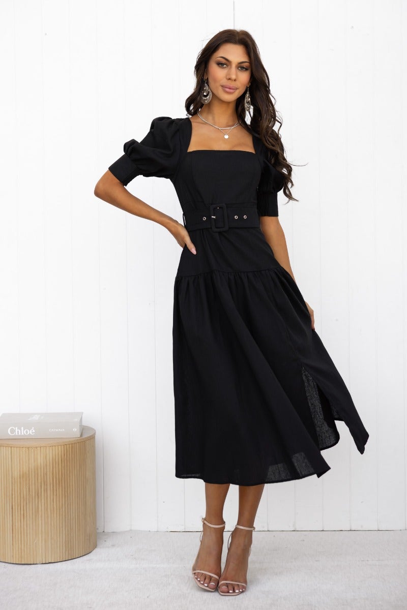 Woman wearing black linen blend Innis Midi Dress with square neckline and fabric belt, showcasing elegant design.