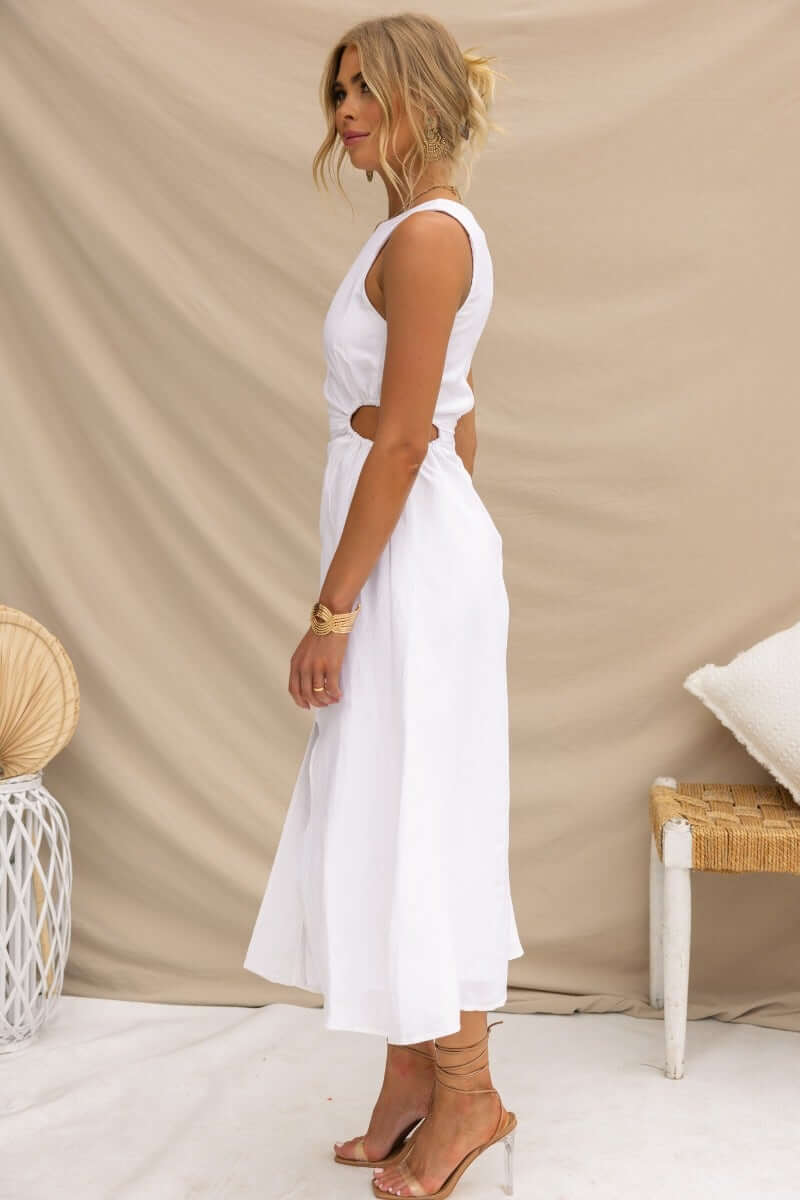 Side view of Rozita Midi Dress in white, featuring a round neckline, cut-out sides, and front slit, styled with minimalist accessories.