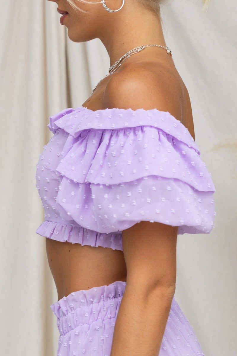 Rosalia Top in lavender with off-shoulder neckline and ruffled sleeves, featuring textured material and a zip at the back.