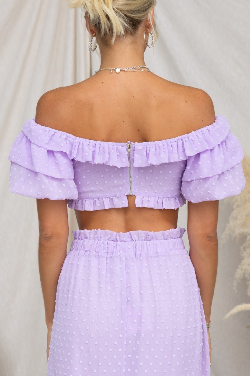 Back view of a lilac Rosalia Top featuring off-shoulder ruffled sleeves and a zip closure, styled with a matching skirt.