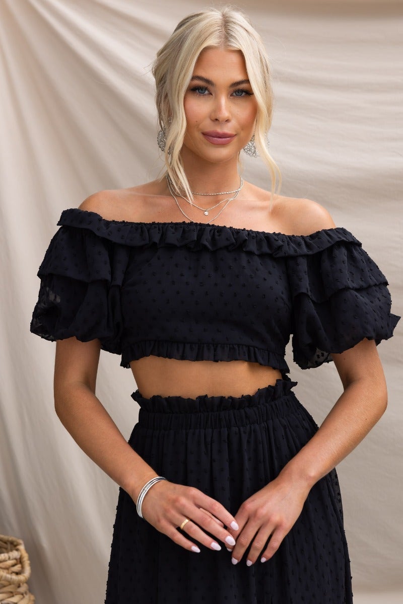 Black textured off-shoulder Rosalia Top with elastic neckline and ruffled sleeves, styled with matching skirt.