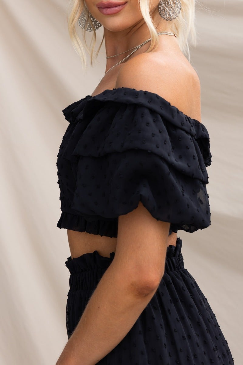Off-shoulder black textured Rosalia top with ruffled sleeves, worn by a model, showcasing a chic, stylish look.