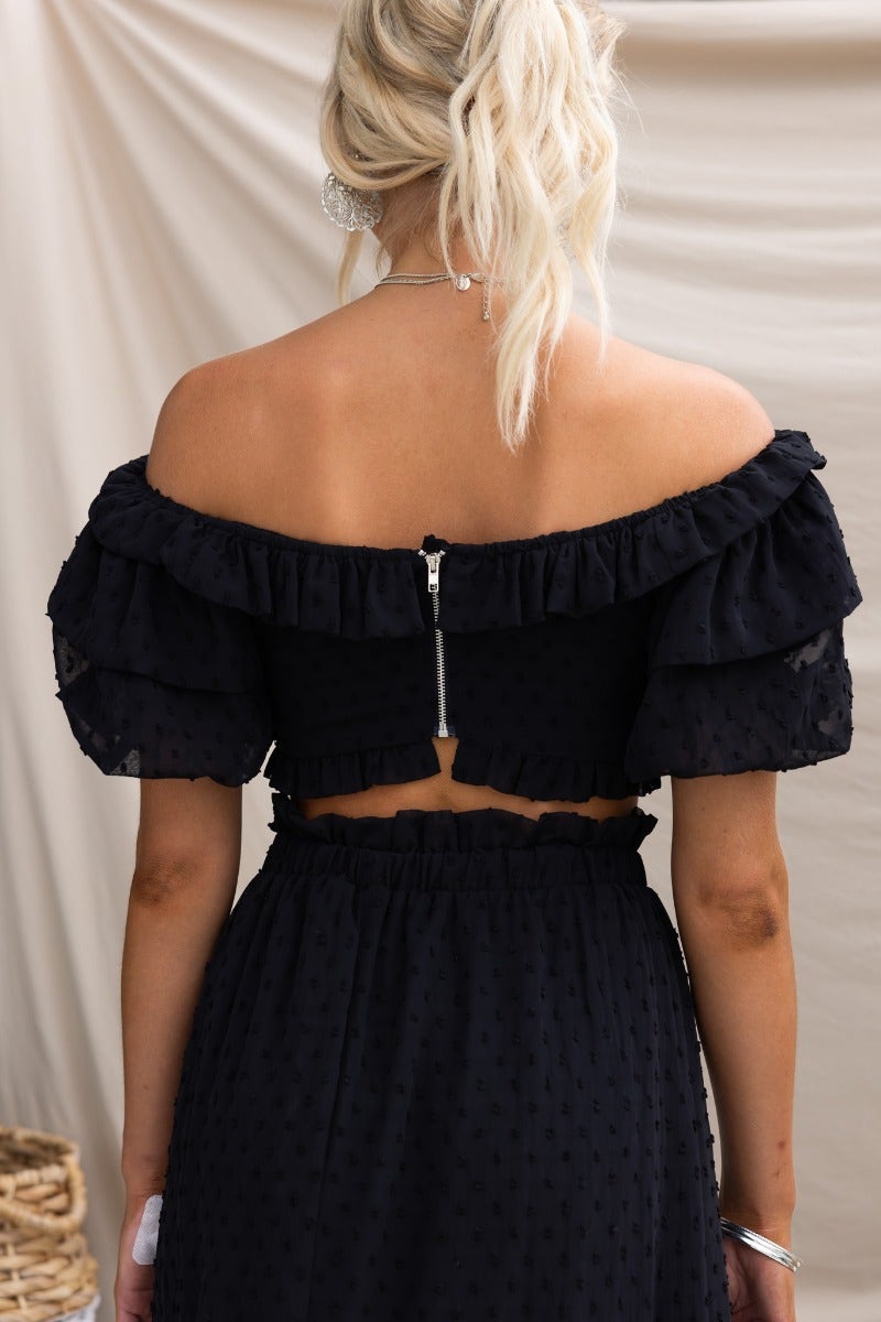 Back view of Rosalia Top featuring an off-shoulder design, ruffled sleeves, and a zip closure in black textured fabric.
