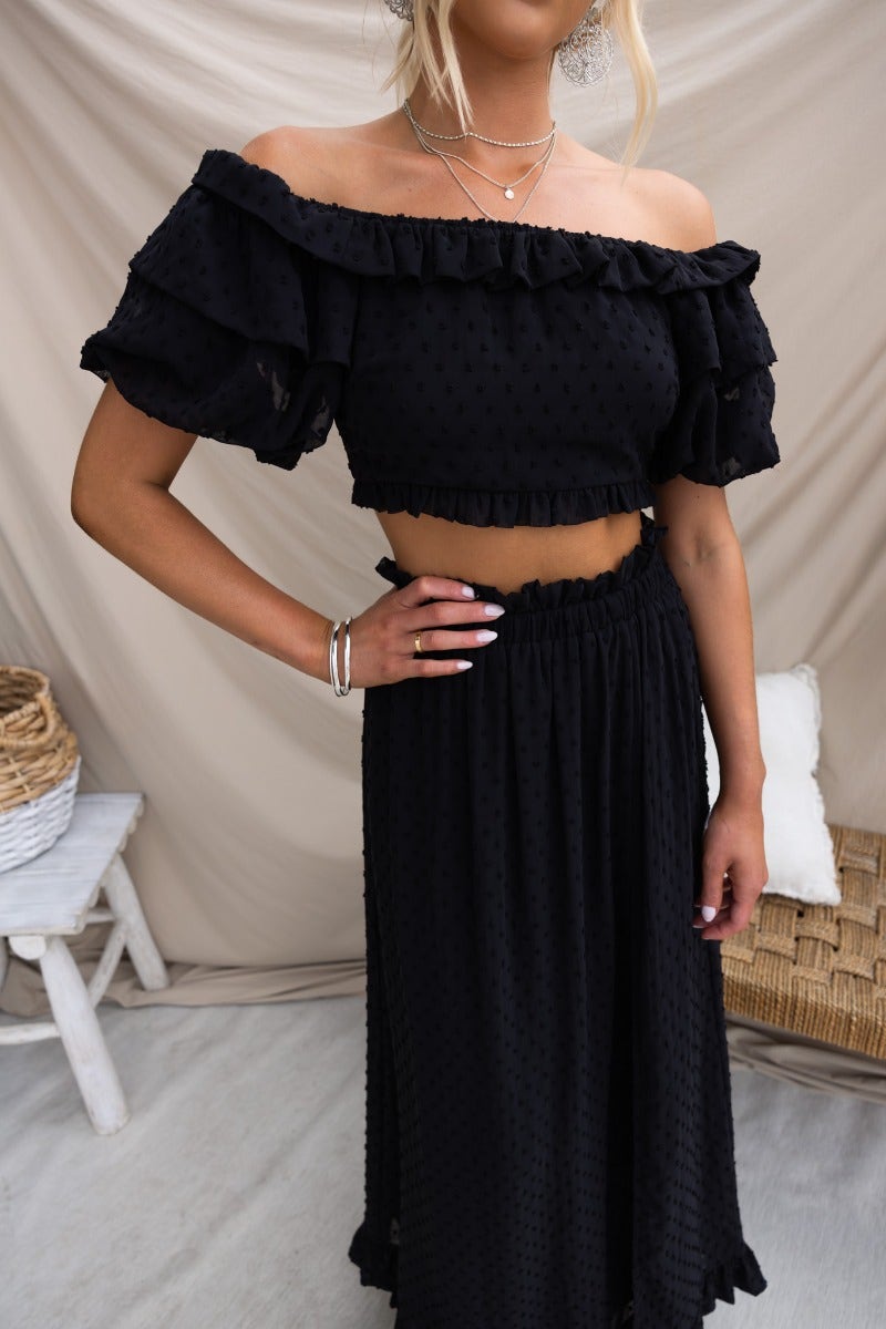 Stylish off-shoulder black textured Rosalia top paired with a matching skirt, featuring ruffles and elastic detail.