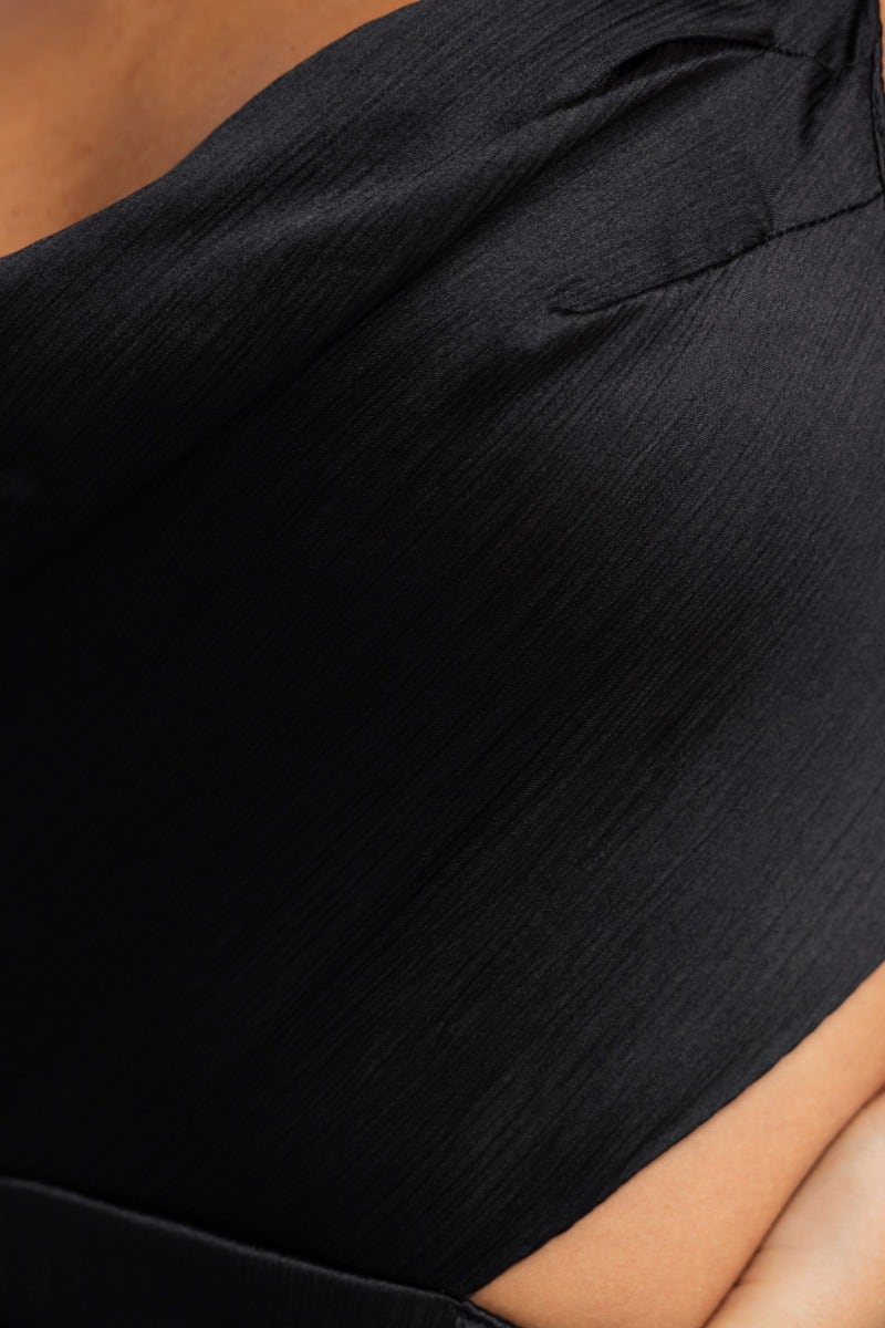 Close-up of a black textured dress featuring a cowl neckline and draping material, ideal for elegant occasions.