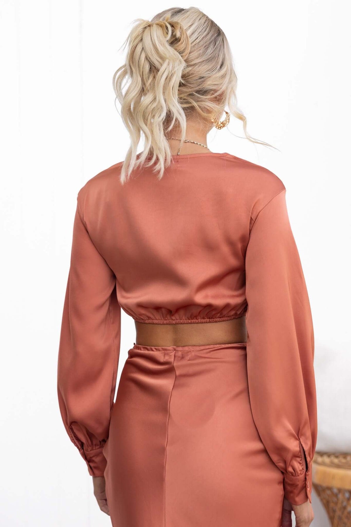 Back view of the Serene Top in satin fabric, featuring a cropped design with elastic waistband and long sleeves.