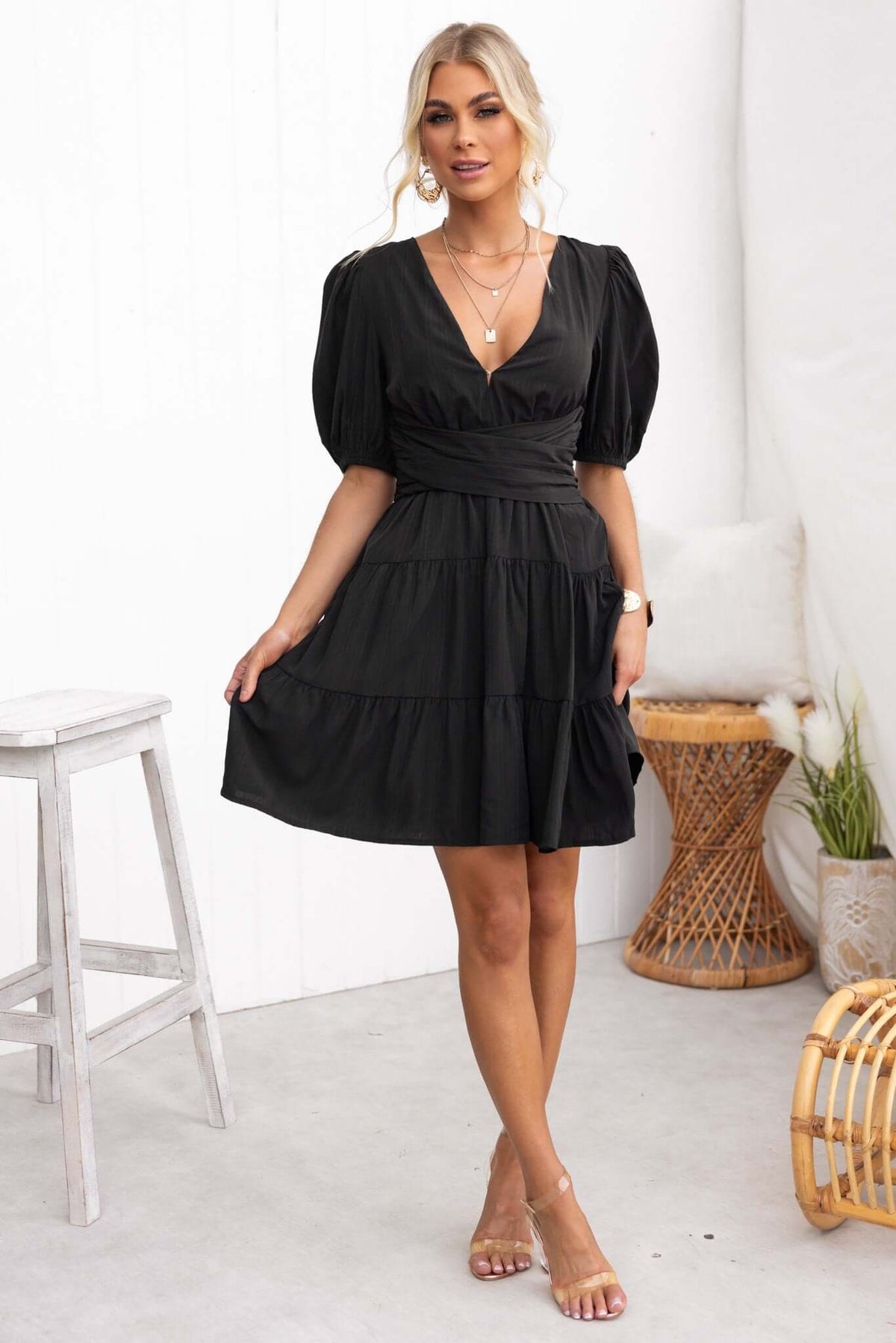 Model wearing the Sakura Dress, a trendy black V-neckline dress with puff sleeves and tiered skirt.