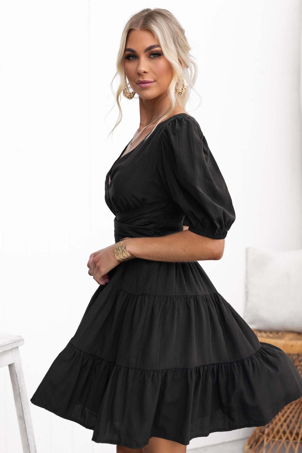 Model wearing a black Sakura dress with a V-neckline and puff sleeves, showcasing its elegant tiered design.