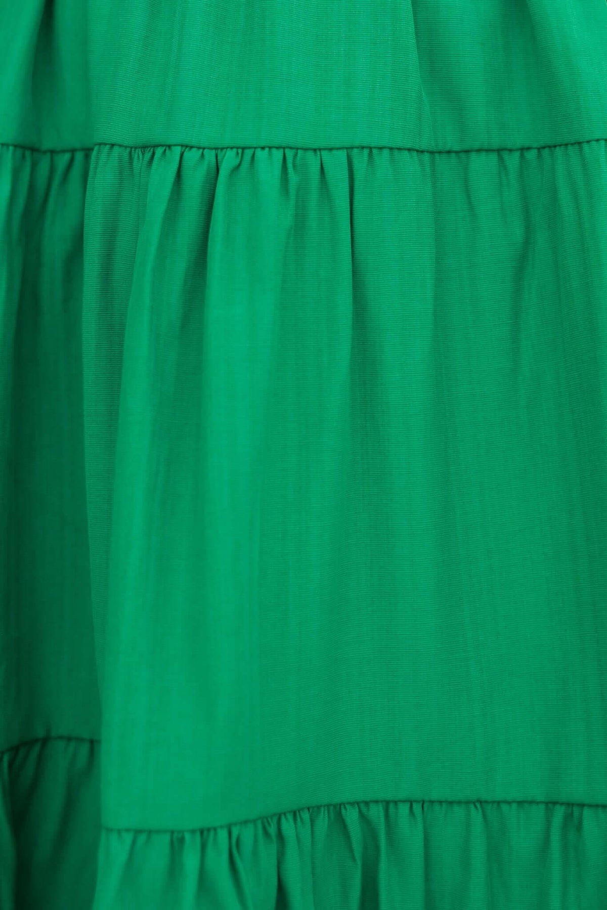 Close-up of the green fabric of the Sakura Dress, featuring a tiered ruffle design and smooth texture.