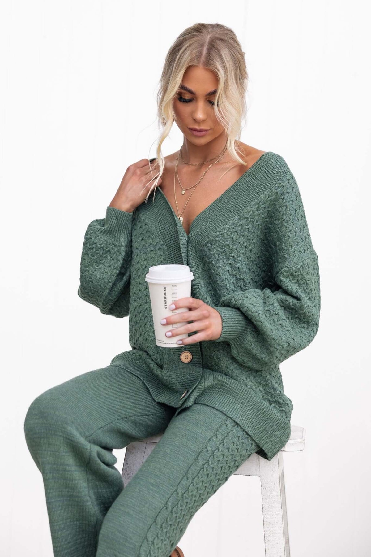 Model wearing a green Jesse Cardigan with a V-neckline, holding a coffee cup, styled in a relaxed fit.