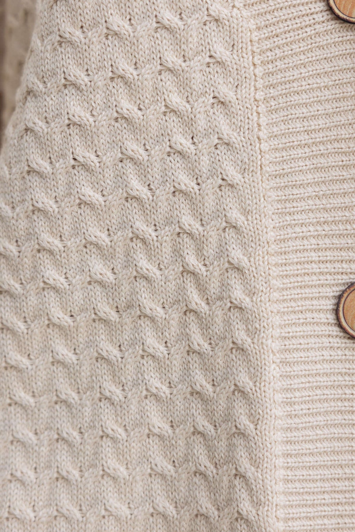 Close-up of a textured beige knit fabric with wooden buttons, showcasing a cozy and stylish design.