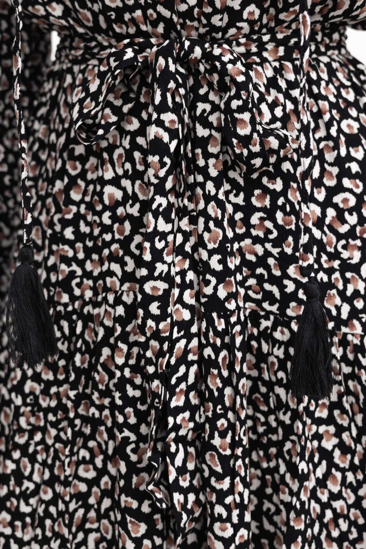 Close-up of Maura Midi Dress showcasing black and tan leopard print fabric with a tied belt and tassels.