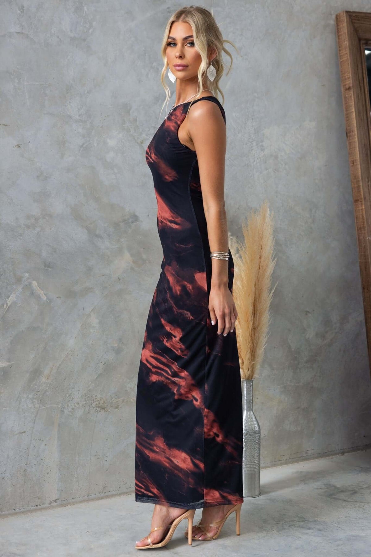Model in a stylish black maxi dress with abstract colors, showcasing a chic side view against a textured backdrop.