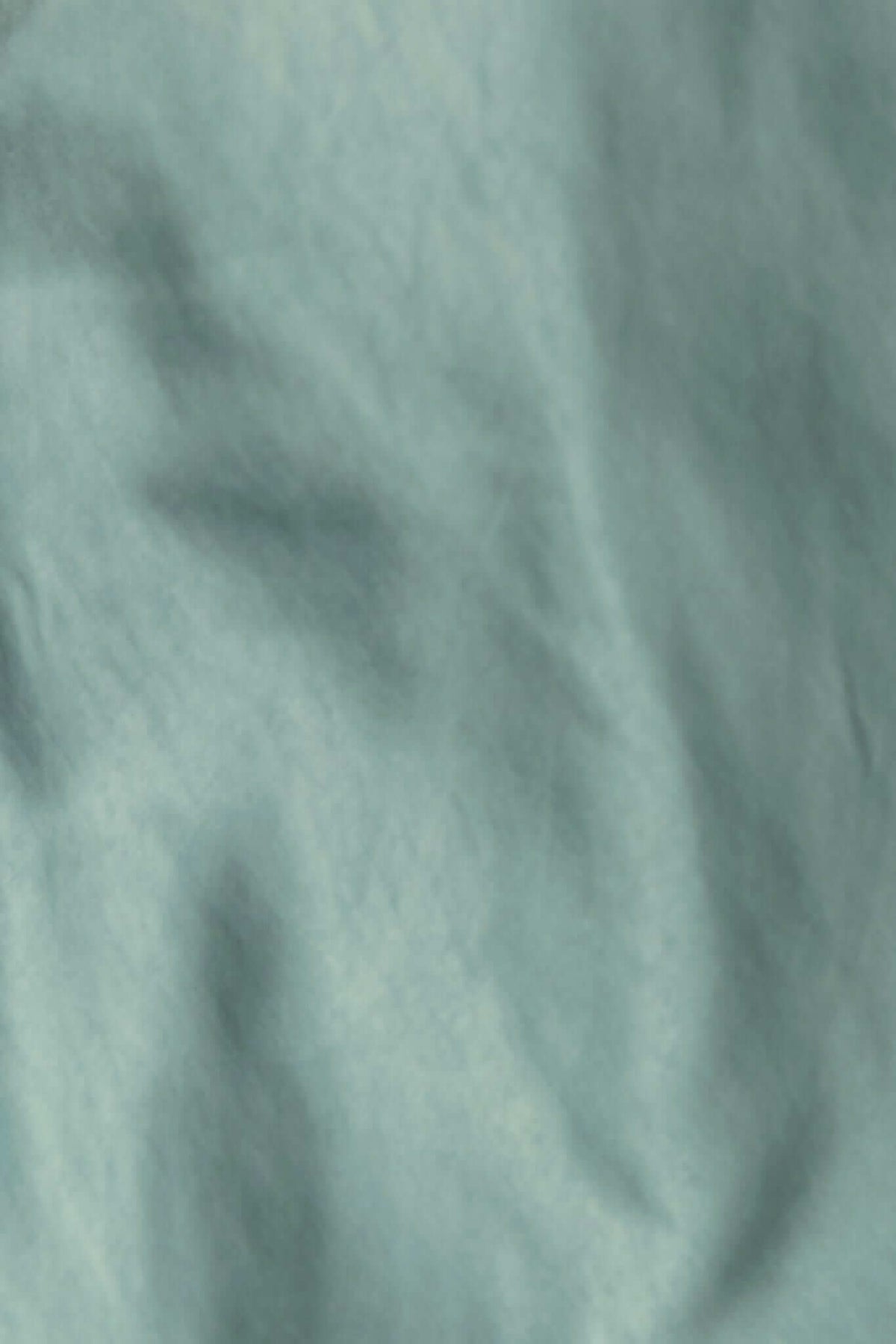 Close-up of smooth, textured fabric in muted teal, showcasing its soft, non-stretch material for comfortable wear.