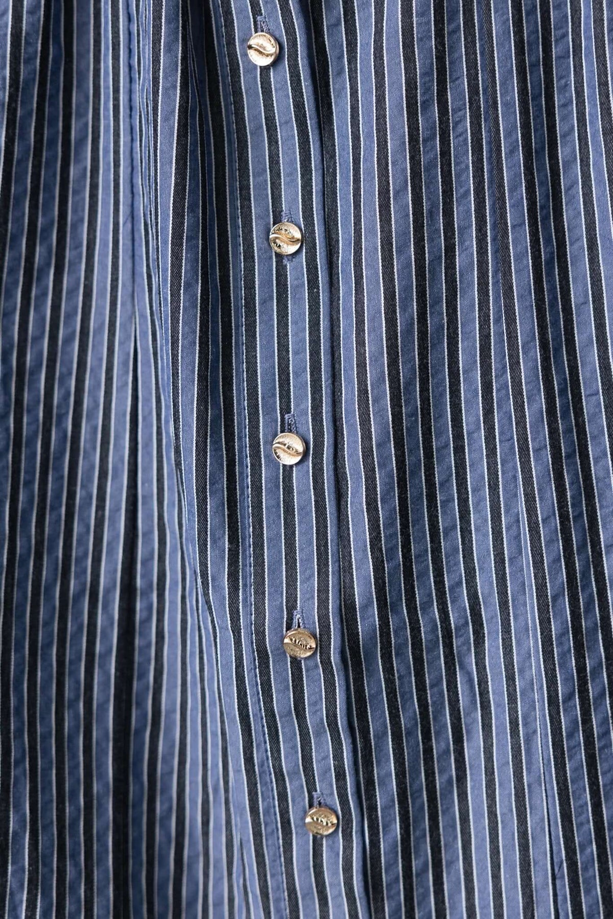 Close-up of a button-up front on a blue and white striped maxi dress fabric.