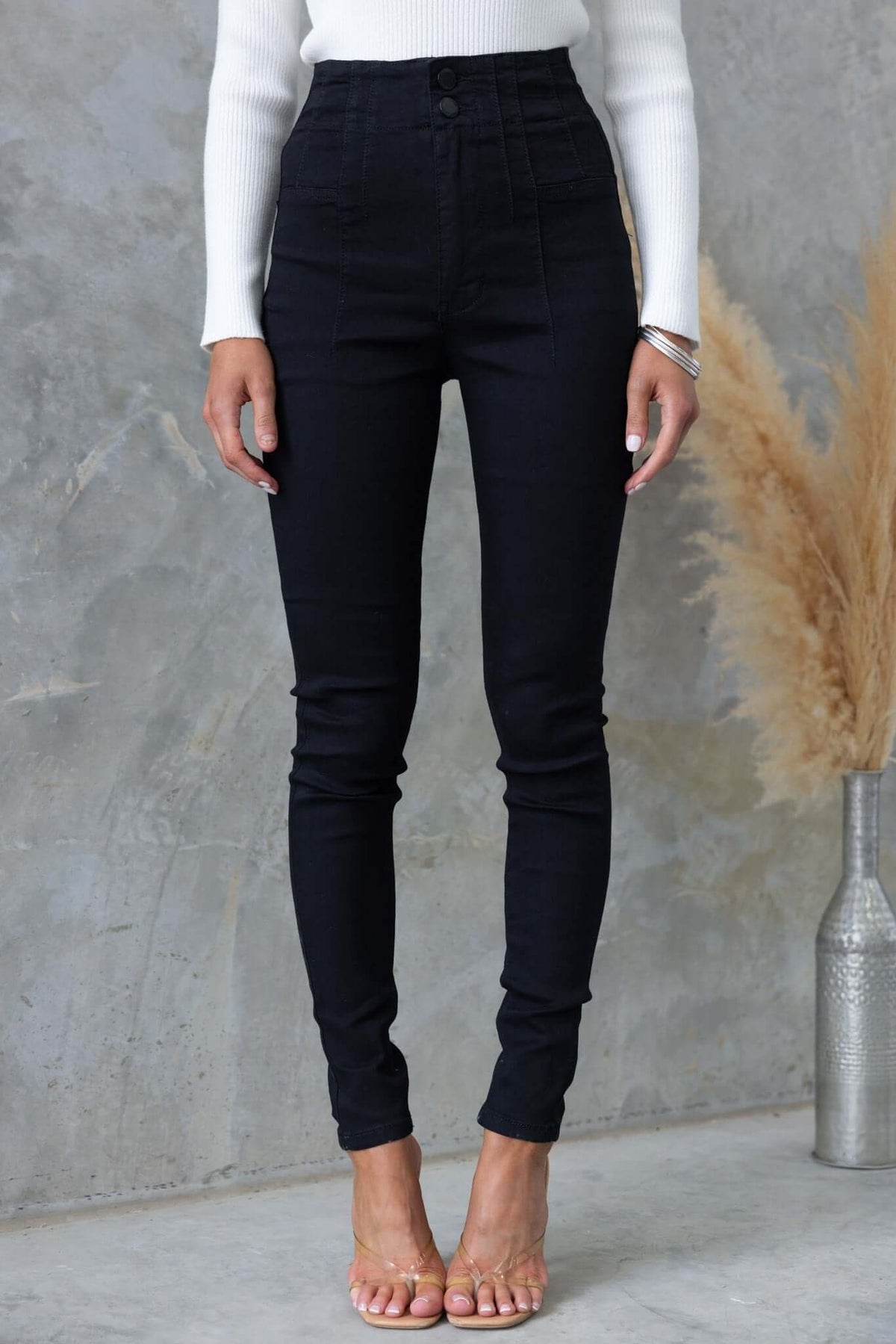 Model wearing Okara Black Denim Jeans with mid-high waist fit and skinny style against a textured backdrop.