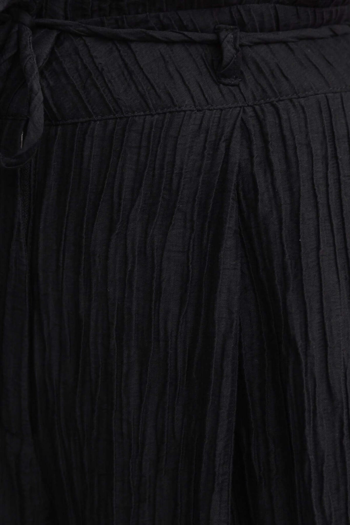 Close-up of black textured pants with removable tie and pleated detail.