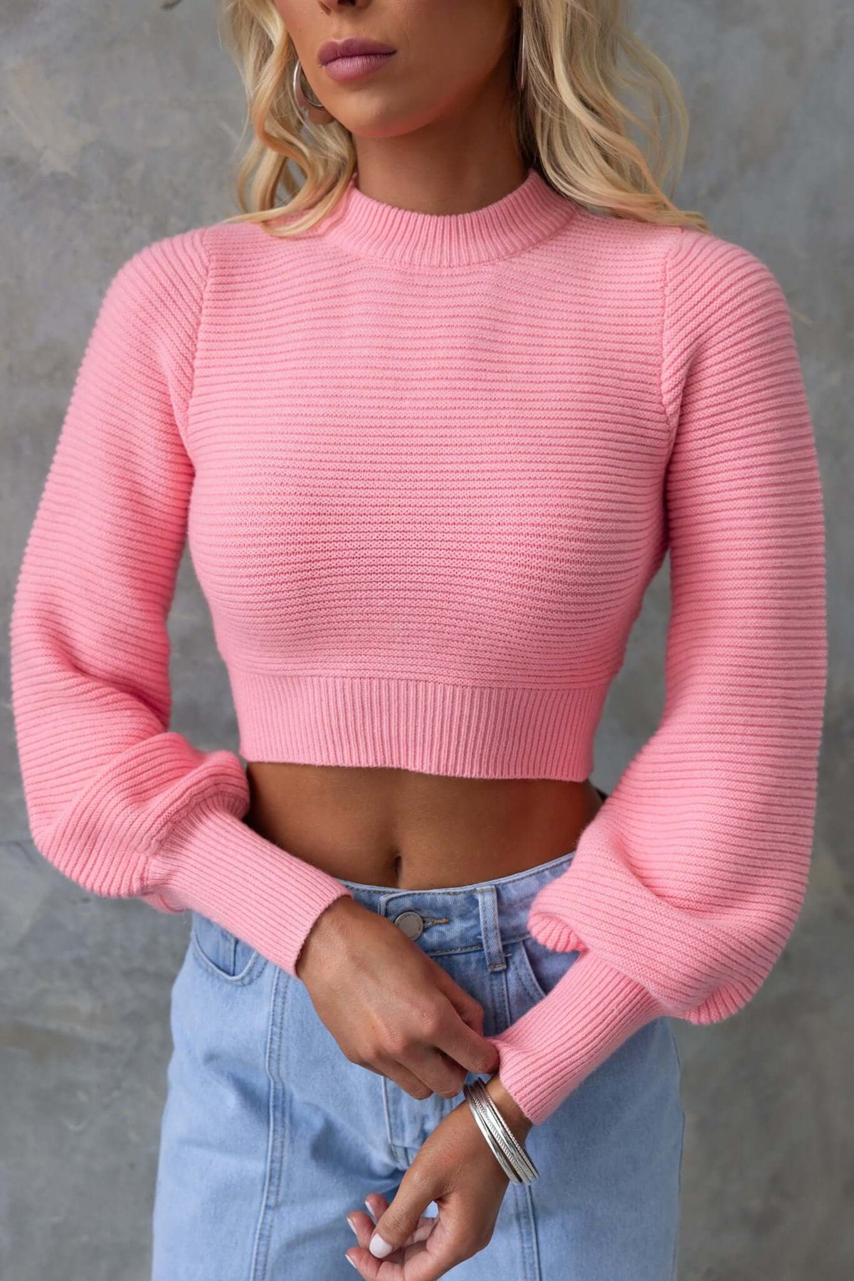Model wearing a pink Reba Jumper with high neckline and bell sleeves, styled with high-waisted denim.