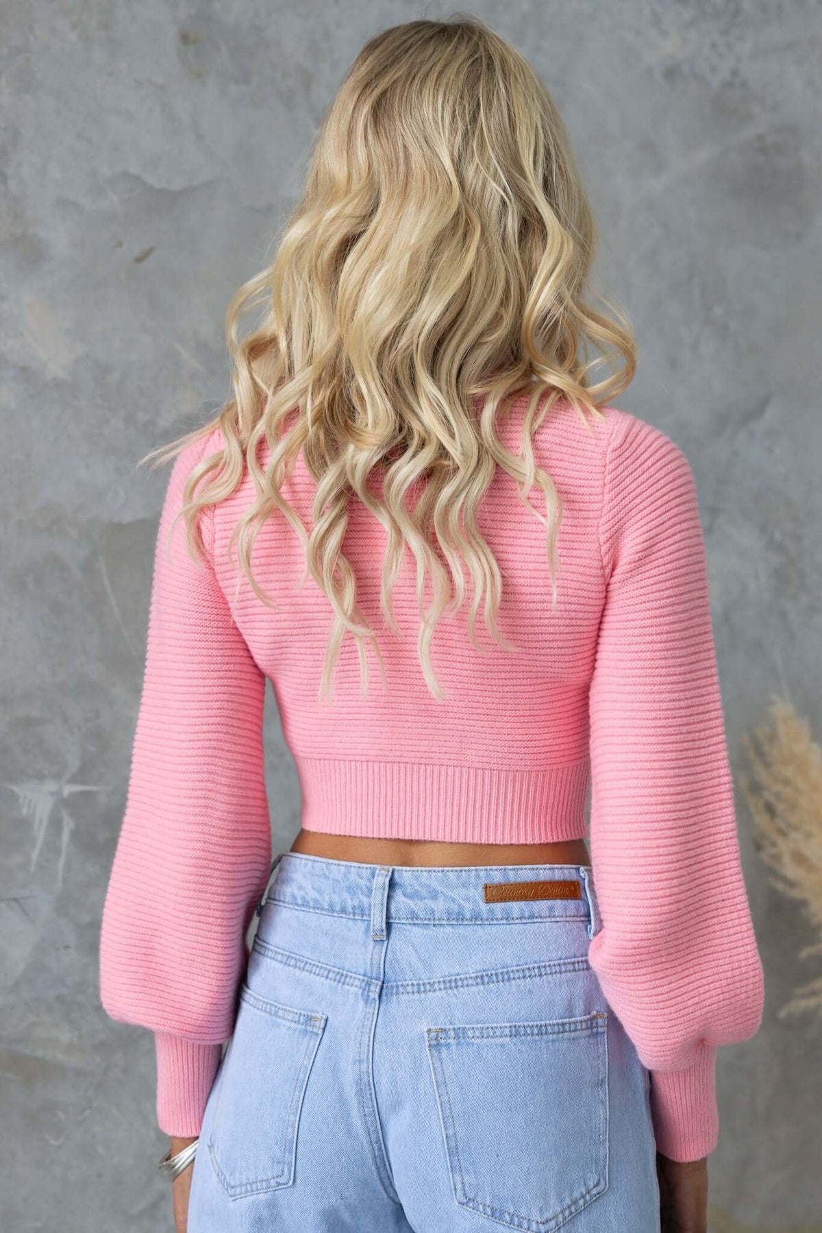 Back view of a pink Reba Jumper with bell sleeves, styled with high-waisted denim jeans.