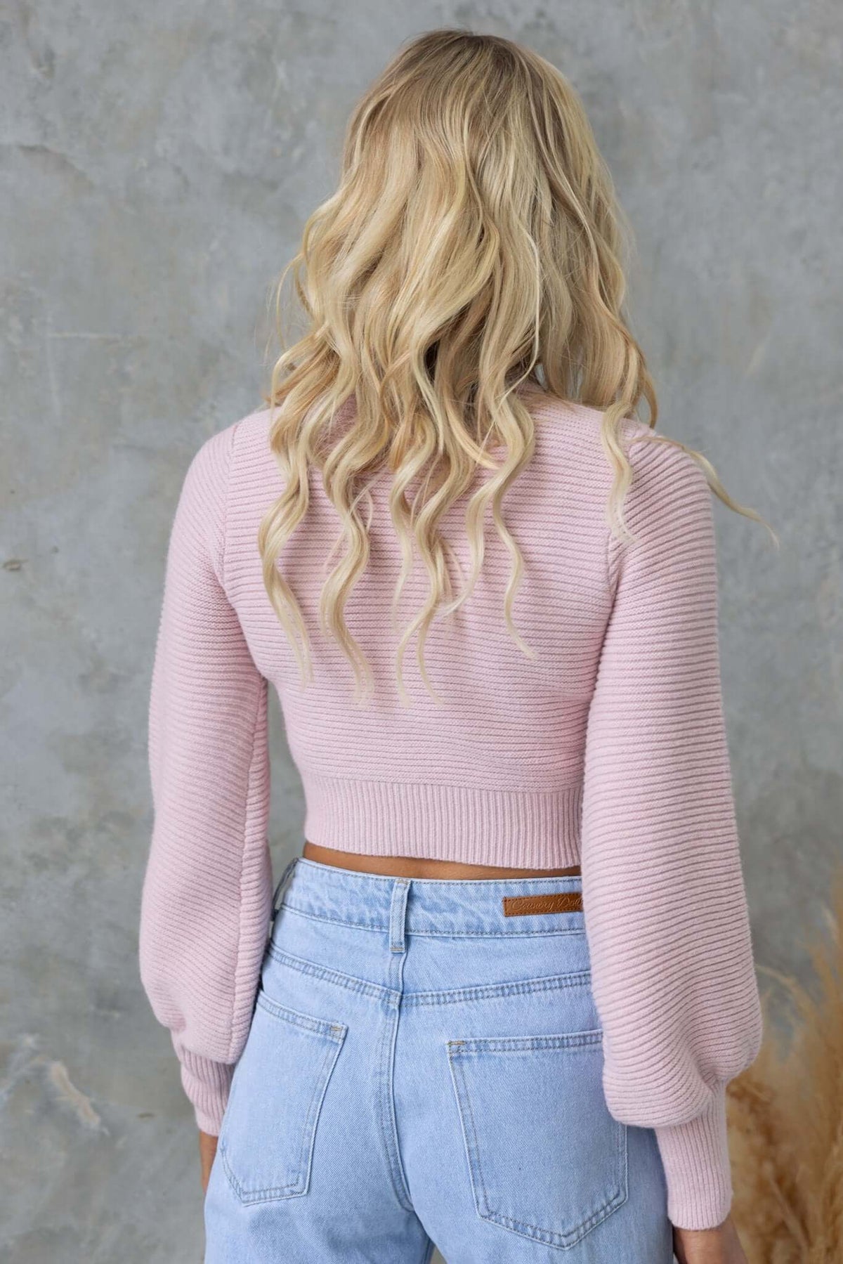 Back view of a woman wearing a pink Reba Jumper with bell sleeves and a ribbed knit texture.
