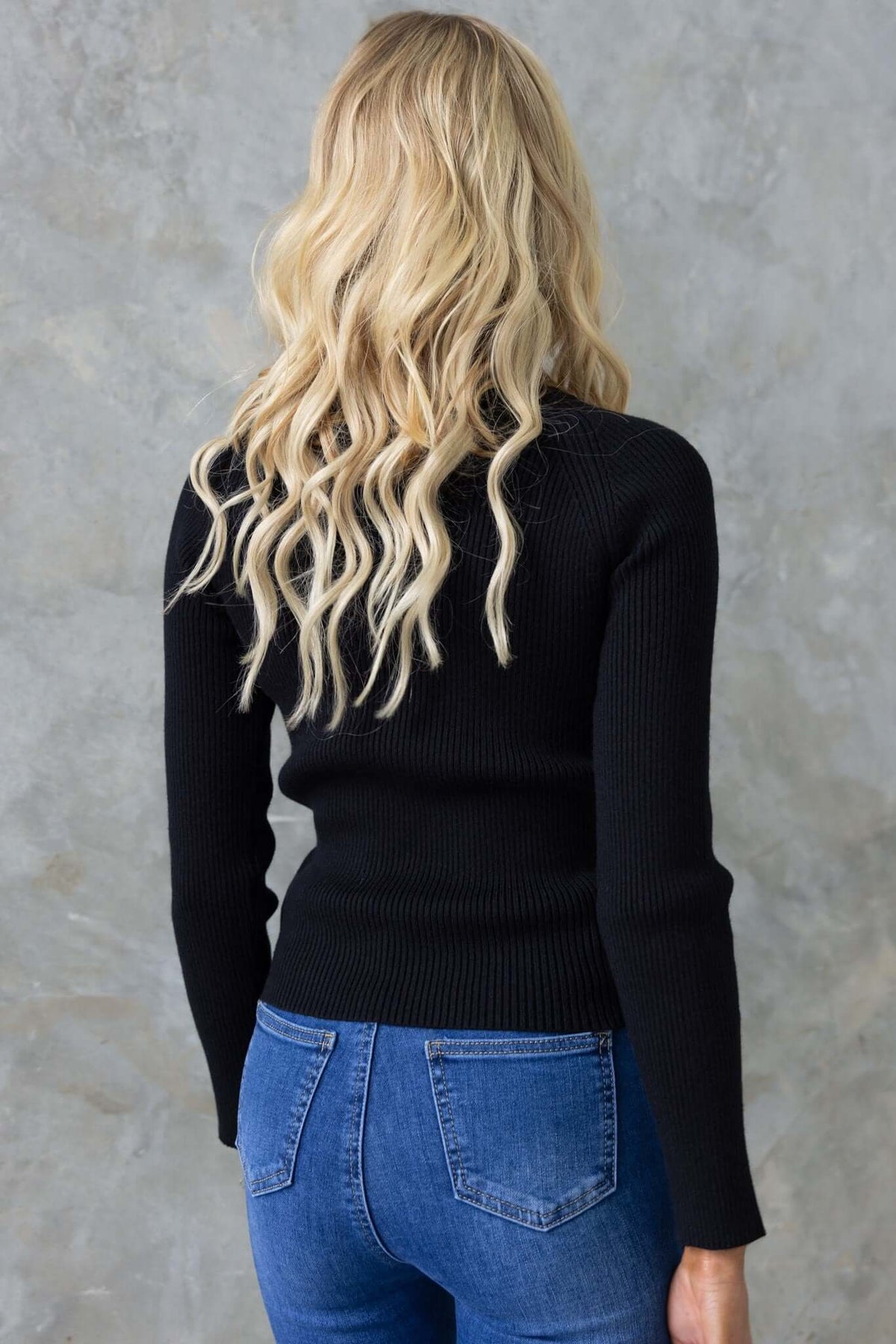 Back view of a model wearing the Avola Top, a fitted black ribbed knit top with a round neckline.