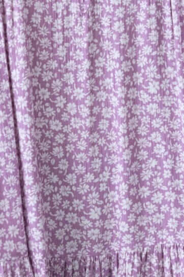 Purple floral fabric of the Fossa Dress featuring delicate white flowers and a ruffled hem.