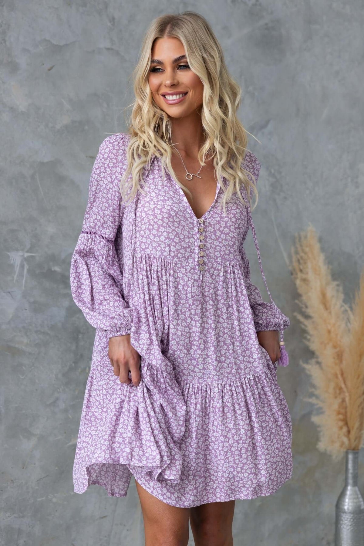Model wearing Fossa Dress in lavender floral pattern featuring V-neckline and tie detail.