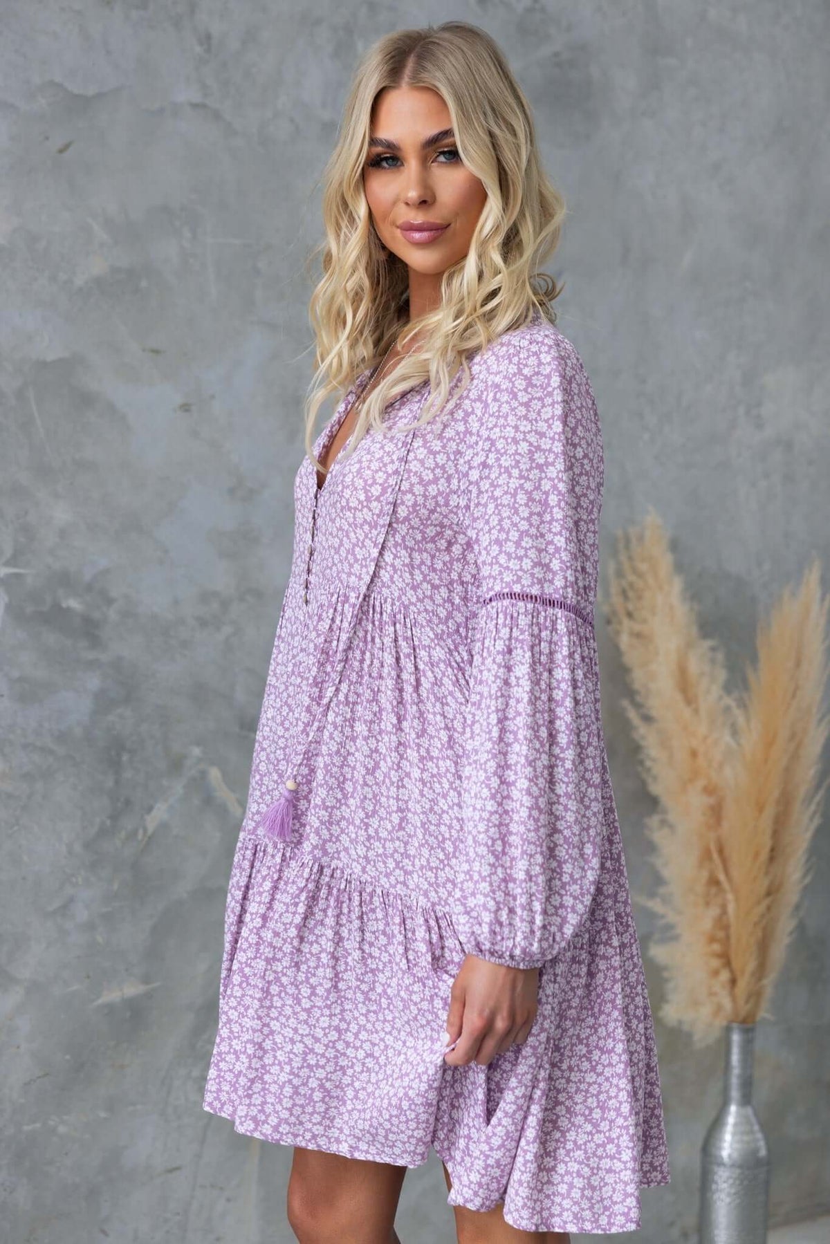 Model wearing the Fossa Dress, a relaxed lilac floral dress with V-neckline and tie detail.