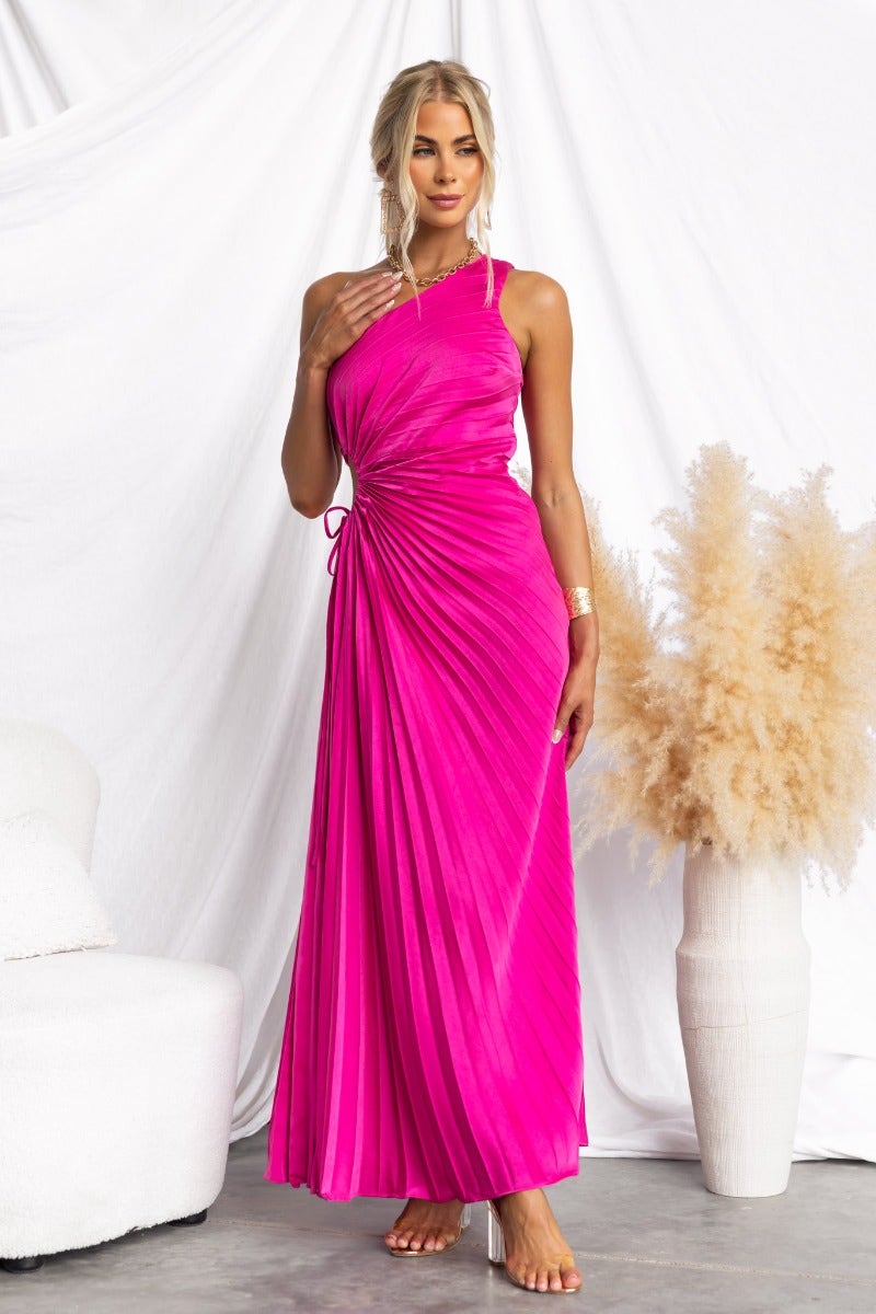 Model wearing a pink Ottile Maxi Dress with one-shoulder neckline and pleated design, featuring a cut-out waist and adjustable tie.