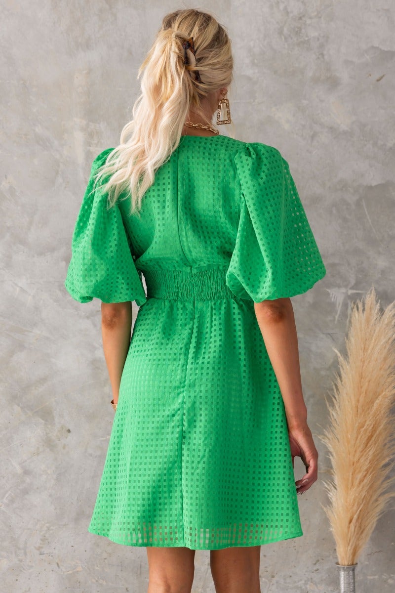 Model showcasing the back of a green Lantier mini dress with puff sleeves and elastic waist.