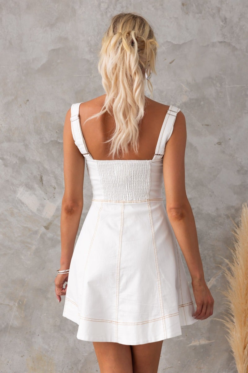 Back view of a white Fitzroy denim dress featuring adjustable straps and smocked elastic detail.