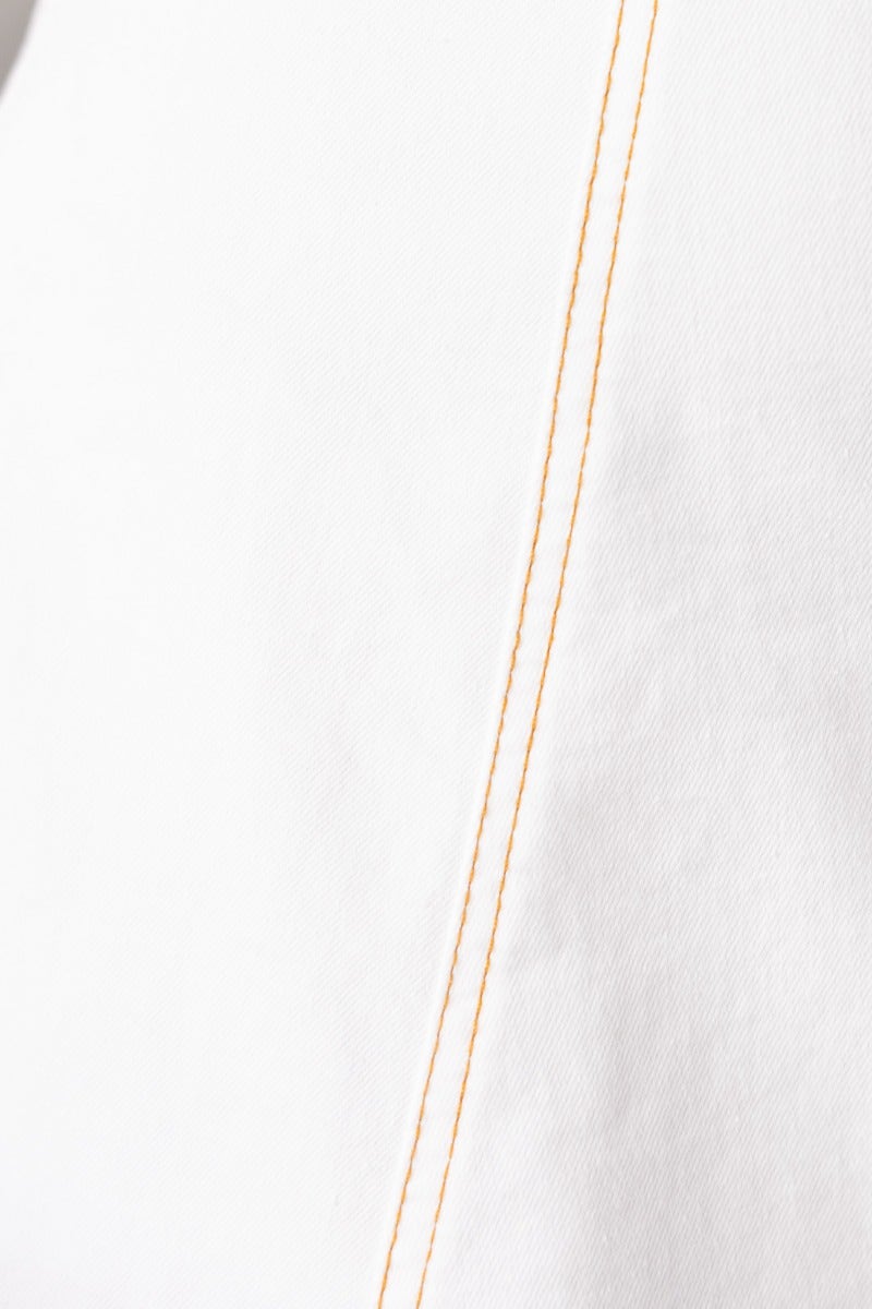 Close-up of white fabric showcasing yellow stitching details, highlighting the quality and design features.