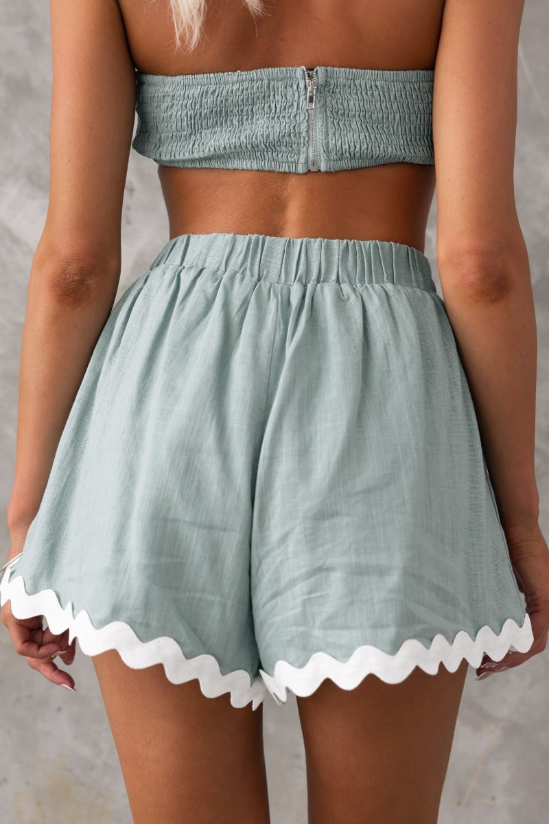 Back view of Take It Easy Shorts featuring a mid-high waist, elastic waistband, and scalloped hem in a light mint color.