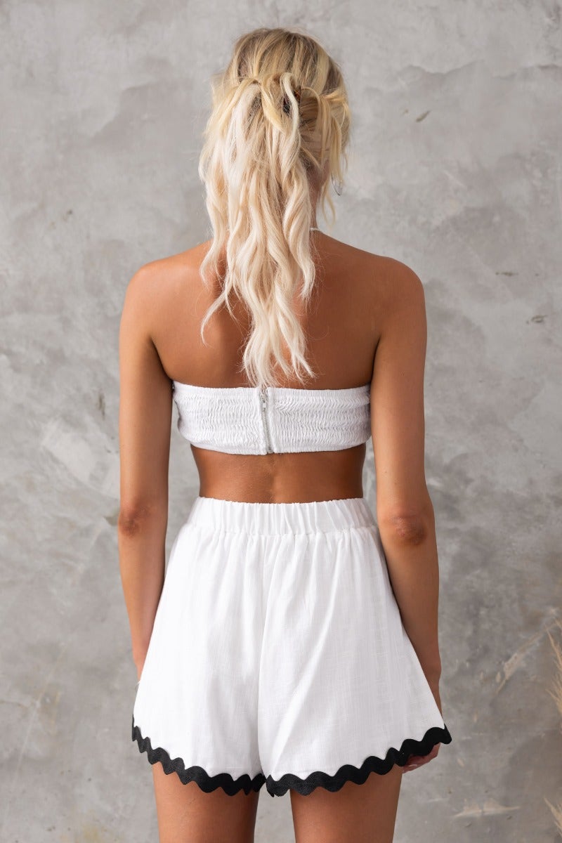 Model showcasing the Take It Easy Top, a strapless, smocked back top paired with white shorts, featuring a lined and non-stretch design.