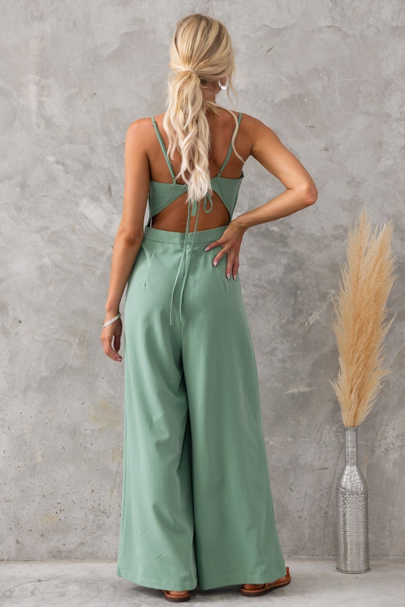 Back view of the Greta jumpsuit showcasing adjustable straps, tied back, and soft green material.