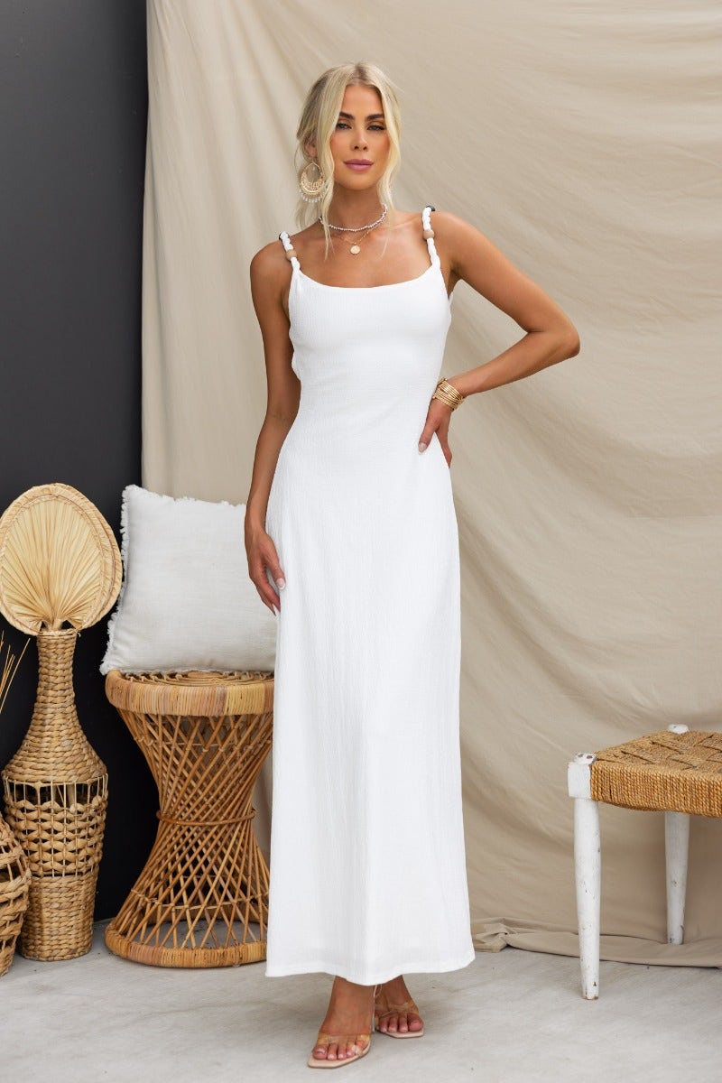 Model wearing a white Ranley maxi dress with bead detailing and an elegant silhouette, posed elegantly in a serene setting.