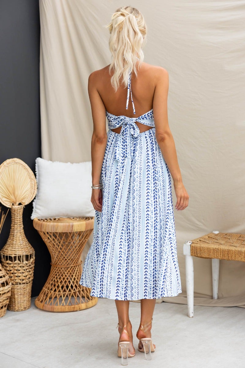 Back view of model in Qano Midi Dress with abstract print, adjustable tie neckline, and pockets, showcased in a stylish setting.