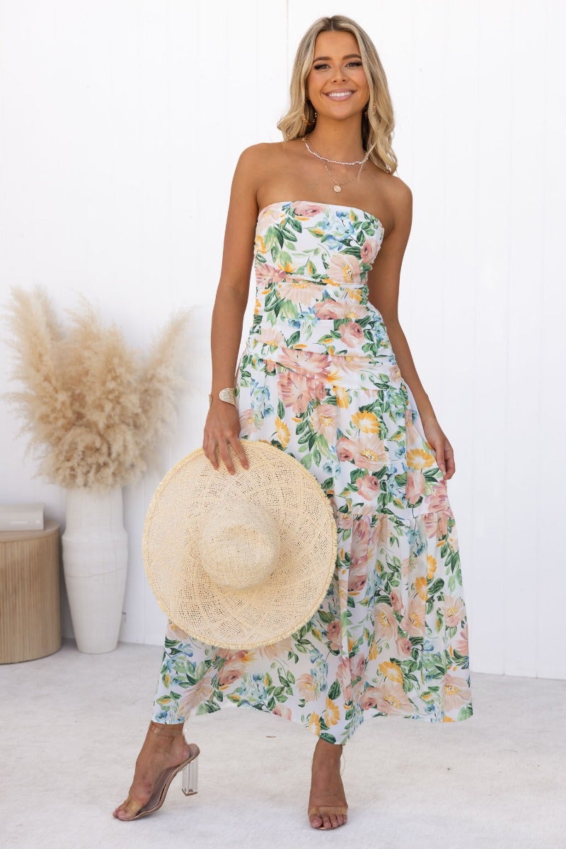 Model wearing a strapless floral Blaine Maxi Dress, holding a straw hat, perfect for summer occasions.