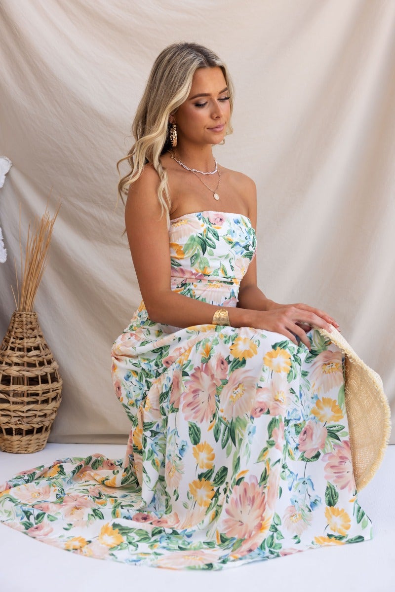 Strapless floral maxi dress featuring a colorful pattern, model sitting gracefully against a neutral backdrop.
