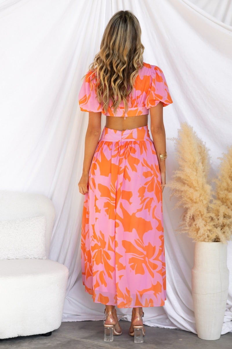 Back view of a woman in a floral print pink and orange Marleen Maxi Dress with cut-out waist and puff sleeves.