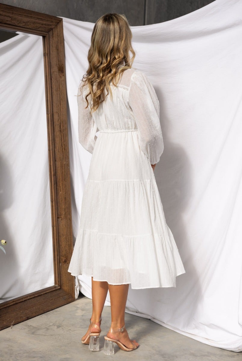 Rear view of a woman wearing a white cotton midi dress with a tiered skirt, styled with a drawstring waist.