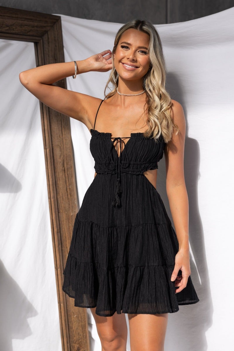 Model wearing a Spirited black dress with adjustable straps, elastic neckline, and tie detail at the bust.